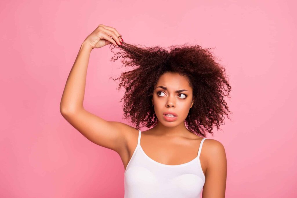 woman holding up a piece of her curly hair and looking at it