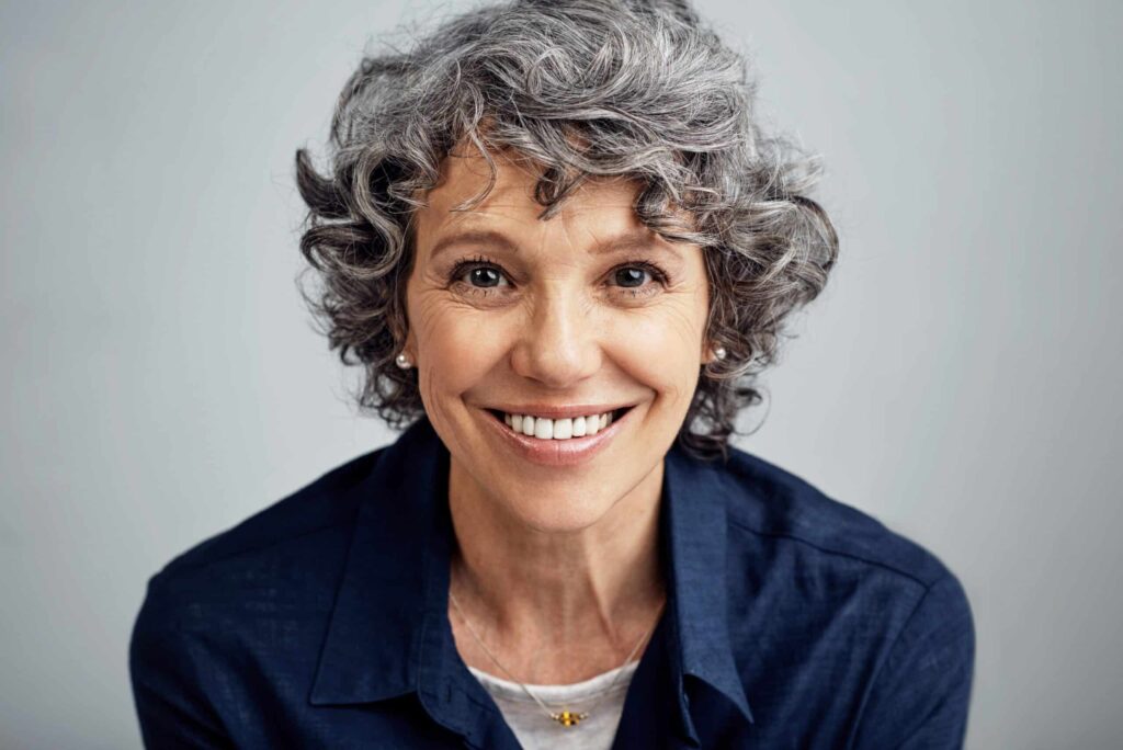 happy mature woman posing against a gray background